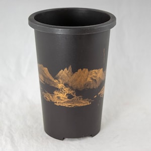 May include: A black plant pot with a gold mountain landscape design. The pot is cylindrical with a slightly flared rim and a flat base. The mountain scene is painted in a detailed, artistic style.