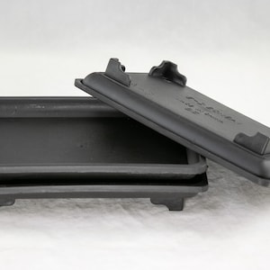 May include: Three black plastic square plant trays stacked on top of each other. The top tray has a raised lip around the edge and four small feet on the bottom.