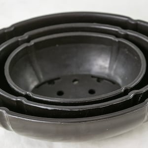 May include: Three black plastic plant pots, nested inside each other, with drainage holes in the bottom of the smallest pot.