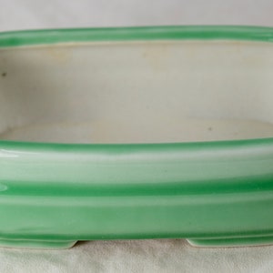 May include: A green ceramic rectangular planter with white stripes. The planter has a smooth, glazed finish and a slightly rounded bottom.
