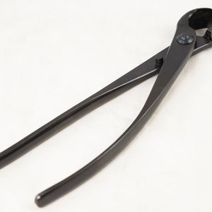 May include: Black bonsai shears with a curved blade and a spring-loaded handle. The shears are designed for pruning and shaping bonsai trees.