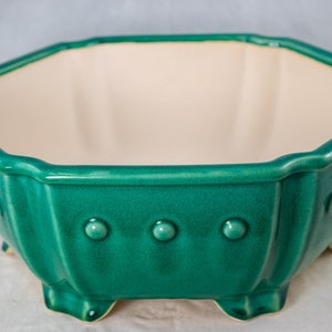 May include: A green octagonal ceramic planter with a white interior and a textured, dotted exterior. The planter has a wide, shallow base and a flared rim.