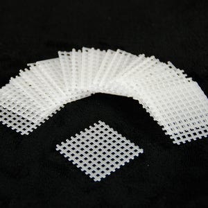 May include: A collection of white plastic canvas sheets arranged on a black background. The sheets are rectangular with a grid-like pattern, suitable for various crafting projects. One square sheet is separate.