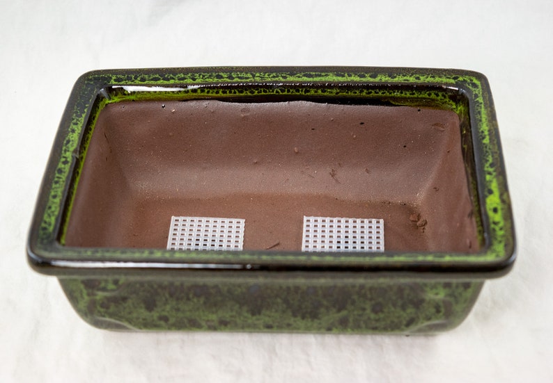 May include: A green glazed rectangular ceramic bonsai pot with two white plastic mesh squares inside.