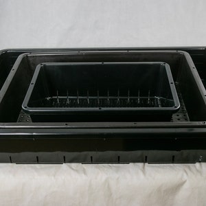 May include: Three black plastic trays of varying sizes, stacked inside each other. The trays have a textured surface and drainage holes.