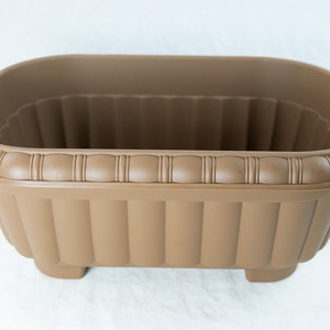 May include: A brown rectangular plastic planter with a decorative rim and ribbed sides. The planter has four small feet.