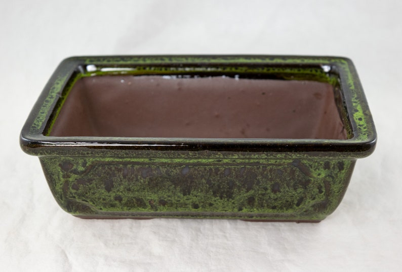 May include: A rectangular green and brown ceramic bonsai pot. The pot has a glazed finish and a slightly raised rim.