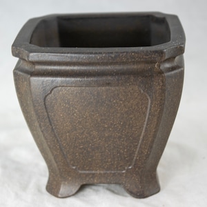 May include: A square, dark brown ceramic bonsai pot with a textured surface and four feet. The pot has a slightly flared rim and a rectangular opening.