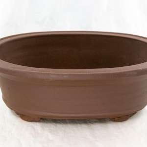 May include: A brown oval ceramic bonsai pot with three small feet.