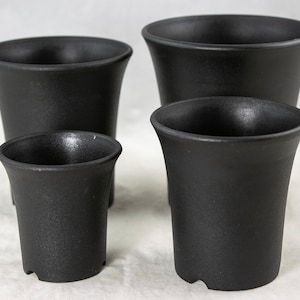 May include: Four black plastic pots of varying sizes. The pots are all round and have a flared lip. They are ideal for planting small plants or succulents.