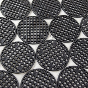 May include: A close-up of a group of black plastic circular mesh coasters. The coasters are arranged in a grid pattern.