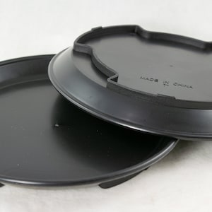May include: Two black plastic plant saucers stacked on top of each other. The top saucer has the words "Made in China" printed on the bottom.