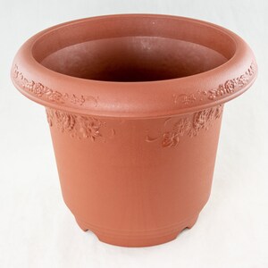 May include: A brown plastic flower pot with a wide rim and floral detailing. The pot has a slightly tapered shape and is designed for planting flowers or other plants. The pot is made of durable plastic and is suitable for both indoor and outdoor use.
