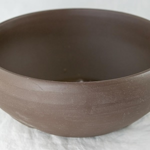 May include: A large, brown ceramic bowl with a smooth, rounded interior and a slightly textured exterior.