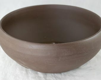 May include: A large, brown ceramic bowl with a smooth, rounded interior and a slightly textured exterior.