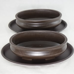 May include: Two brown ceramic oval-shaped plant pots with matching brown saucer trays. The pots have a smooth, slightly textured finish.