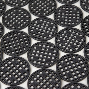 May include: A close-up of a group of black plastic circular coasters with a grid pattern. The coasters are arranged in a staggered pattern.