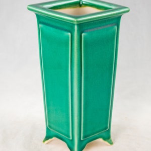 May include: A square green ceramic planter with four legs. The planter has a smooth, glossy finish.