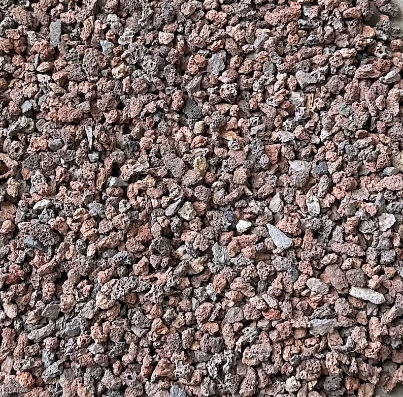 K&ouml;nnte beinhalten: Nahaufnahme eines Haufens kleiner, rotbrauner Lavasteine. Die Steine sind unregelm&auml;&szlig;ig geformt und haben eine raue, por&ouml;se Textur.