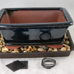 May include: A rectangular bonsai pot with a glossy dark blue exterior and a terracotta interior. It sits on a dark brown rectangular tray filled with smooth, multi-colored river stones. Included are two small black mesh squares and a black wire coil.