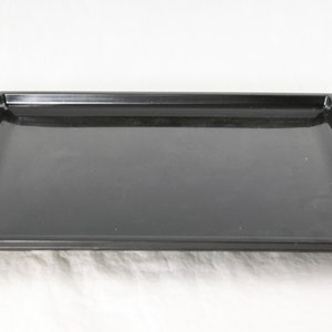 May include: A black rectangular serving tray with a smooth, glossy surface. The tray has a raised edge around the perimeter.