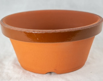 May include: A terracotta flower pot with a brown glazed rim. The pot is unglazed and has a drainage hole.