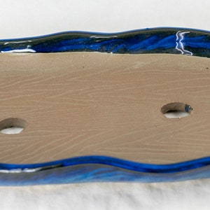 May include: A blue and brown ceramic planter with a wavy edge and three drainage holes. The planter is designed for succulents or other small plants.