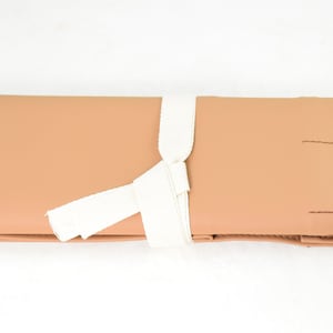May include: A tan leather roll-up case with a white fabric tie. The case has multiple compartments and is ideal for storing and organizing small items.