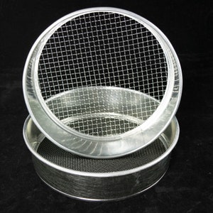 May include: Two silver metal sieves stacked on top of each other. The top sieve has a fine mesh screen and the bottom sieve has a coarser mesh screen.