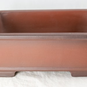 May include: A rectangular brown ceramic bonsai pot with a slightly raised rim and four small feet.