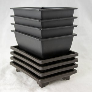 May include: A stack of six black square plastic plant pots with four brown square plastic saucers stacked underneath.