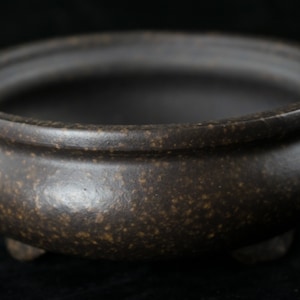 May include: A brown ceramic bonsai pot with a rounded shape and three small feet. The pot has a speckled texture.