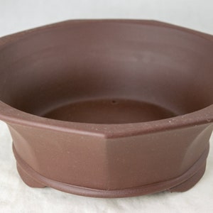 May include: A brown octagonal ceramic planter with a drainage hole. The planter has a rounded bottom and a slightly flared lip.