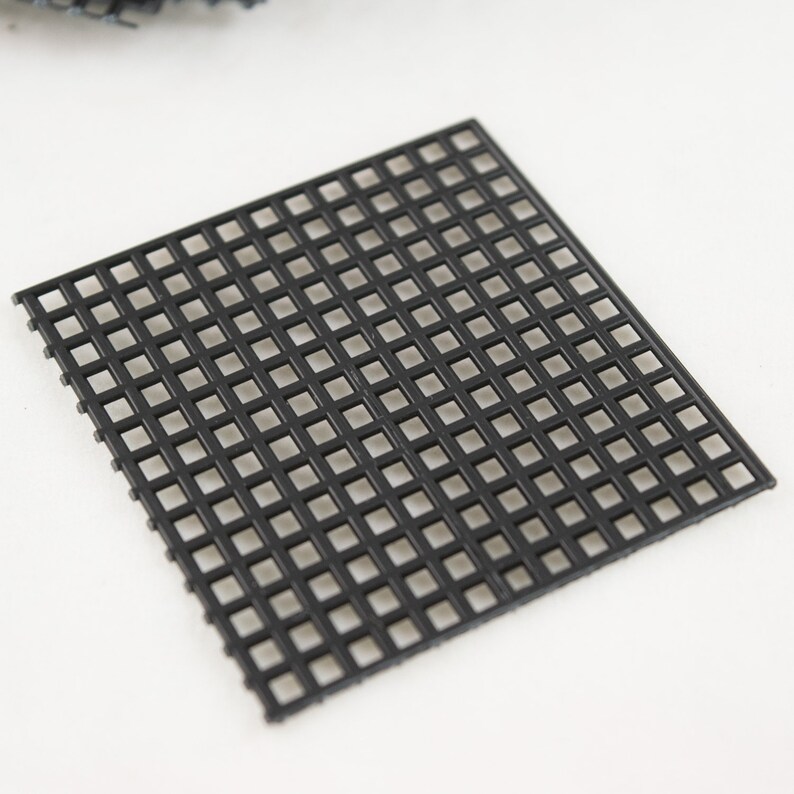 May include: A black plastic square grid with small squares.