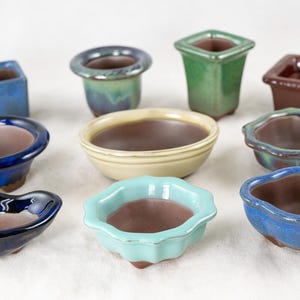 May include: Assortment of ten small ceramic pots in various colors and shapes, including blue, green, brown, and cream. The pots are ideal for small plants or succulents.