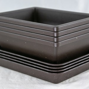 May include: A stack of brown plastic plant pots and saucers. The pots are square and the saucers are round.