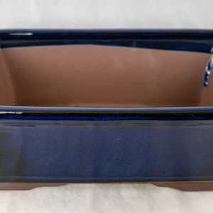 May include: A rectangular blue glazed bonsai pot with a dark brown interior. The pot has a slightly flared rim and a flat base.