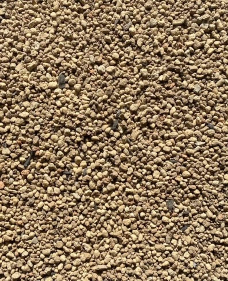 K&ouml;nnte beinhalten: Nahaufnahme einer strukturierten Oberfl&auml;che, die mit kleinen, hellbraunen und beigefarbenen Kieselsteinen bedeckt ist. Die Kieselsteine sind in verschiedenen Gr&ouml;&szlig;en und Formen vorhanden und erzeugen ein nat&uuml;rliches und erdiges Aussehen.