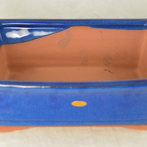 May include: A blue glazed rectangular ceramic bonsai pot with a terracotta interior. The pot has a rounded lip and a slightly flared base.