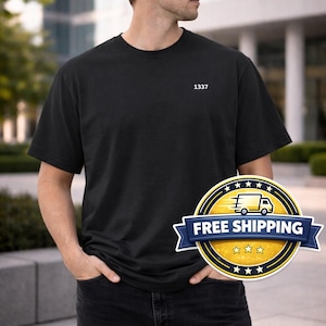 May include: Black short-sleeve t-shirt with the number "1337" printed in white on the upper left chest. The shirt is worn by a person wearing sunglasses and dark jeans. A "Free Shipping" badge is visible.