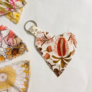 May include: A heart-shaped fabric keyring with a floral design in brown, red, and pink. The keyring has a metal ring and a small fabric loop with a ladybug pattern. Other fabric pieces with floral patterns are visible.