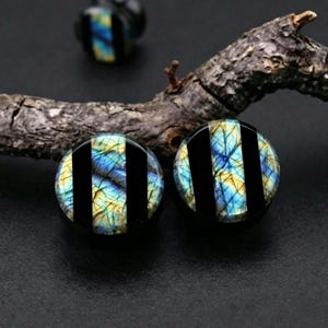 May include: A pair of circular ear plugs featuring a striped design with alternating bands of black material and iridescent labradorite stone displaying blue and yellow flashes with a natural cracked texture across the surface.