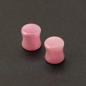 Pode incluir: Dois tamp&otilde;es de ouvido rosa com uma superf&iacute;cie lisa e polida. Os tamp&otilde;es t&ecirc;m uma forma cil&iacute;ndrica com uma borda ligeiramente alargada. A cor &eacute; um rosa suave e claro, e parecem ser feitos de um material s&oacute;lido.