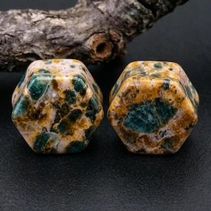 Pode incluir: Dois alargadores hexagonais com um padrão de pedra polida multicolorida com inclusões em azul-petróleo profundo, amarelo-mostarda e creme. A superfície lisa e brilhante apresenta uma textura natural e manchada na forma geométrica de seis lados.