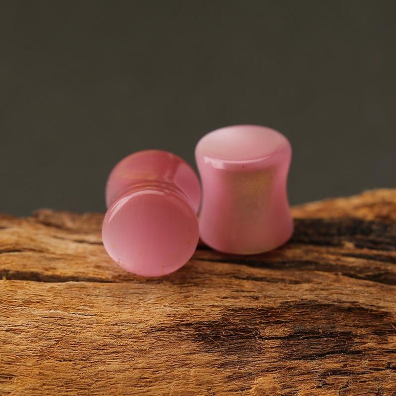 Pode incluir: Tr&ecirc;s tamp&otilde;es de ouvido rosa com formato arredondado. Os tamp&otilde;es s&atilde;o feitos de um material brilhante e s&atilde;o exibidos em um peda&ccedil;o de madeira com um fundo escuro. Os tamp&otilde;es t&ecirc;m uma superf&iacute;cie lisa e polida.