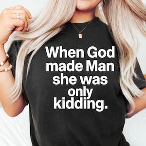 May include: Black t-shirt with the white text: "When God made Man she was only kidding." The shirt has a crew neck and is made of a soft material. The text is centered on the front of the shirt.
