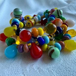 Peut inclure: Un bracelet multi-rangs composé d'une variété de perles en verre colorées de formes sphériques, en goutte d'eau et en disque. Les perles sont dans des tons de rouge, jaune, bleu, vert, orange et violet, entrecoupées de petites entretoises rayées.