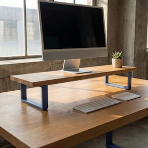 May include: A wooden monitor stand with blue metal legs supports a silver computer monitor. A small potted plant and a wireless keyboard and mouse are on the desk. The desk is made of wood.