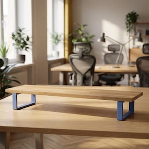 May include: A wooden monitor stand with a rectangular top and blue metal legs. The stand is designed to elevate a computer monitor, providing ergonomic benefits. The stand is made of light-coloured wood.