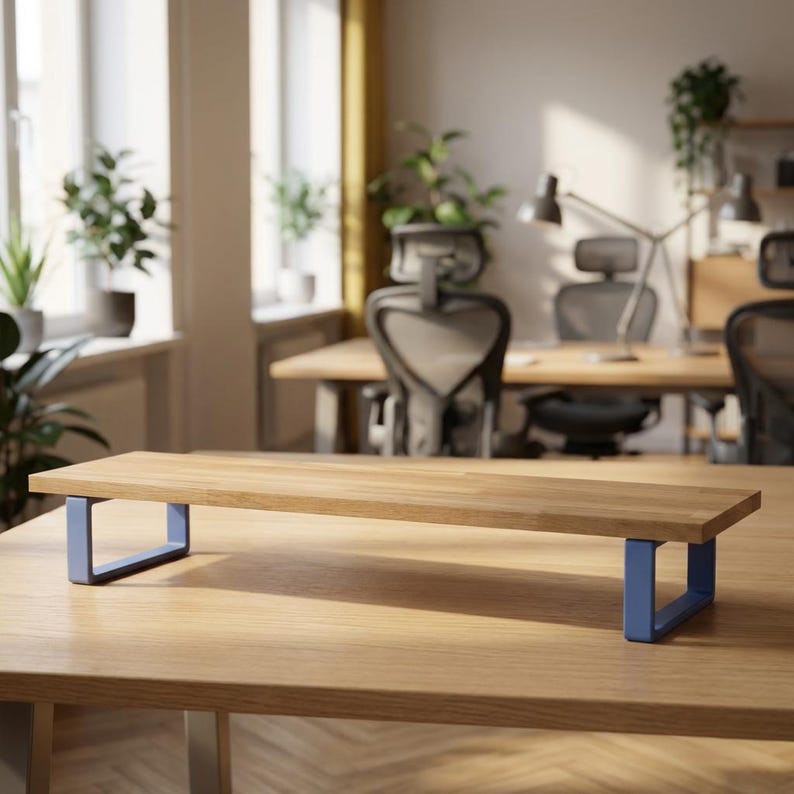May include: A wooden monitor stand with a rectangular top and blue metal legs. The stand is designed to elevate a computer monitor, providing ergonomic benefits. The stand is made of light-coloured wood.